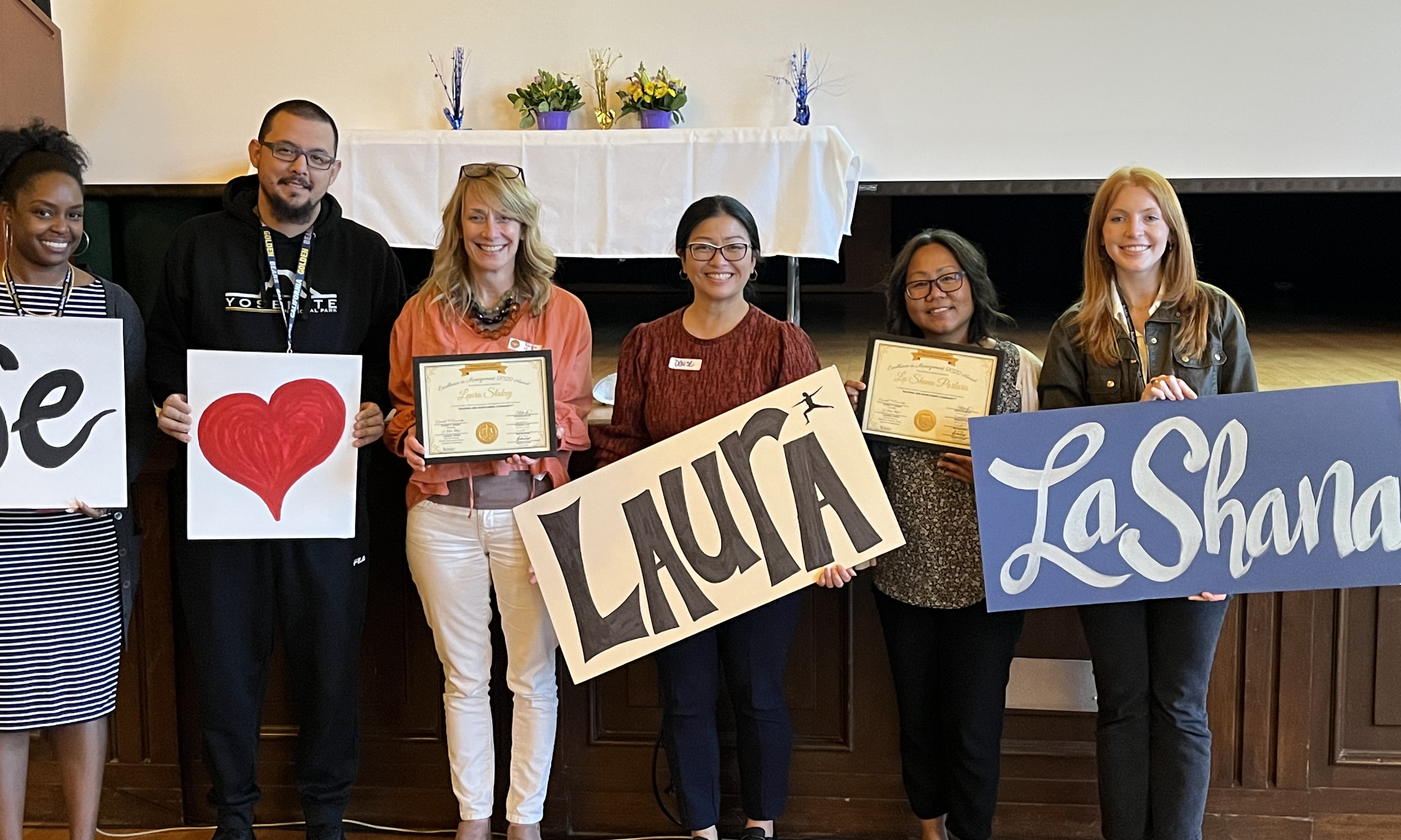 Photo of staff at EIM awards ceremony holding signs we heart Laura La Shana