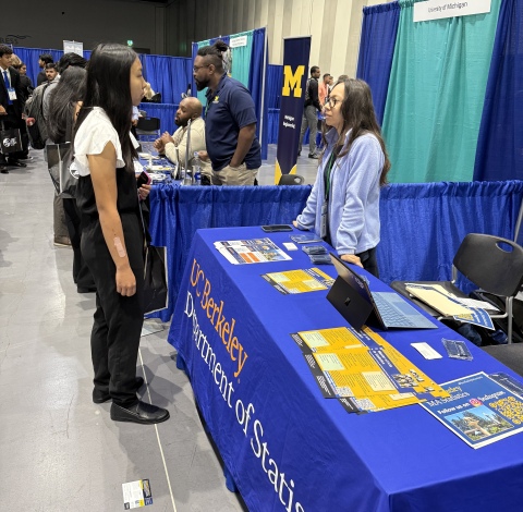 a photo of Hannah Aguilar speaking to another student at the UC Berkeley Department of Statistics booth at GMiS